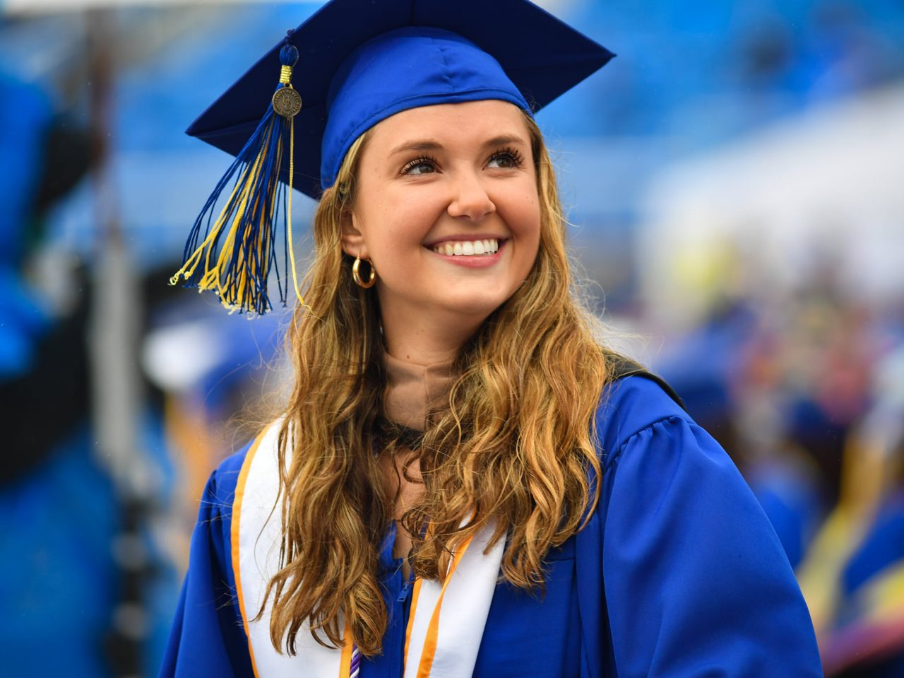 Young woman smiles in her cap and gown at commencement. 