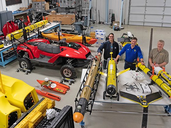 Three researchers pose with a number of underwater robots in a lab.