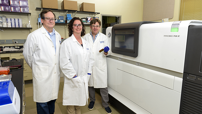 UD researchers stand in front of lab equipment in white lab coats.