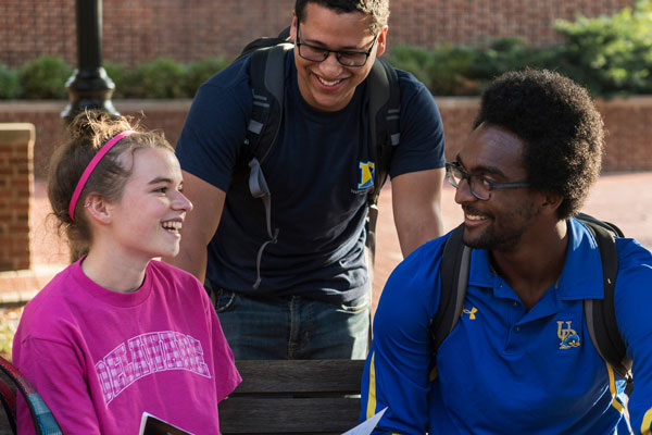Three UD students smile while in conversation with each other. 
