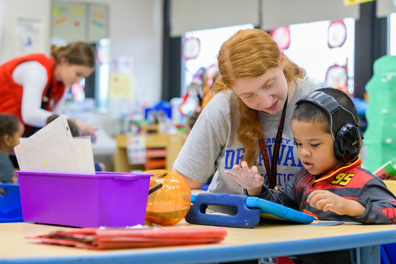 A UD student teacher helps a young boy on a computer tablet in a classroom.