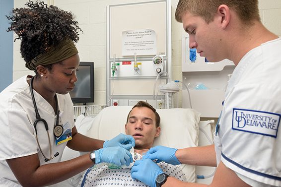 Two UD students in the nursing program learn to provide medical care for a male patient in a hospital simulation.