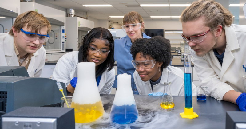 students in white coats observe beakers in a lab on UD's campus. 