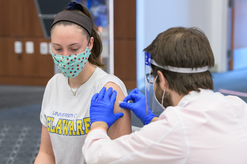 Image of a masked woman receiving a vaccination from a medical professional in a white lab coat 