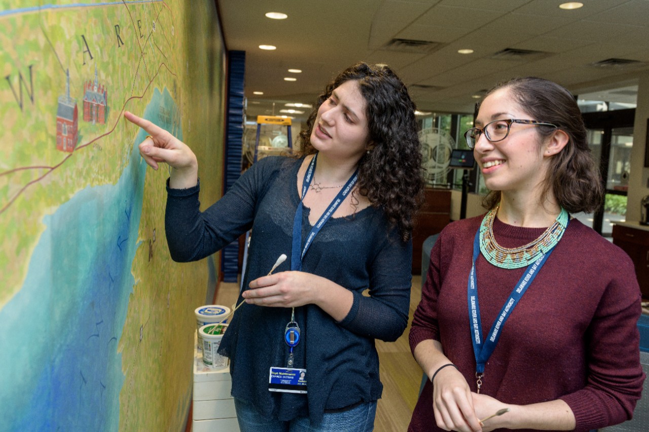 Undergraduate art conservation students Amanda Kasman and Karissa Muratore performing surface cleaning of the so called "Micarta" mural (a brand name for composites of various fabrics in a thermosetting plastic which the mural makes use of) which was recently recovered from storage to become a feature of the newly renovated lobby in the Delaware River and Bay Authority (DRBA) administrative building. Originally painted in 1967 by New York artist Aurion M. Proctor, the mural centers on the Delaware Memorial Bridge and "illustrates metropolitan areas, bridges, tunnels, major highways and historical landmarks over in the mid-Atlantic and New England regions." [DRBA website]. (Evan Krape / University of Delaware)