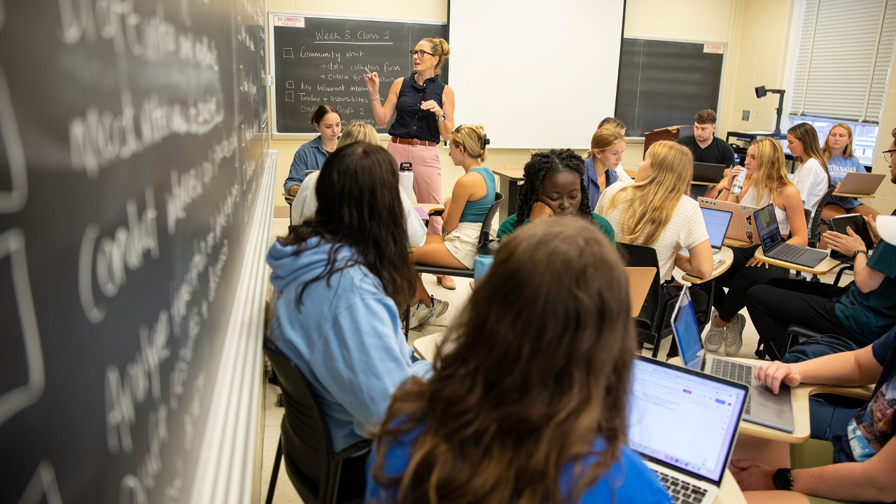 CHS-BHAN_HBS_Development_Health_Promotion_Programs-091522 Students in a classroom working on laptops with chalkboards covered in teaching notes.