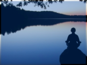 Background photo of a person meditating by a lake in the evening.