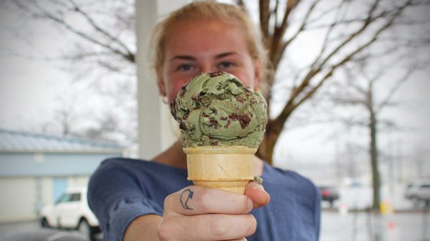 A photo of a student holding an ice cream cone with a scoop of green mint chocolate chip ice cream.