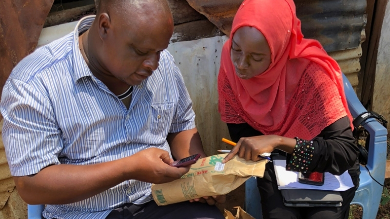 Former Borel Fellow Mariam Gharib (right) helps a Kenyan farmer verify the corn seed’s authenticity by submitting the certification code listed on the seed packet to the manufacturer via a text from his cell phone.