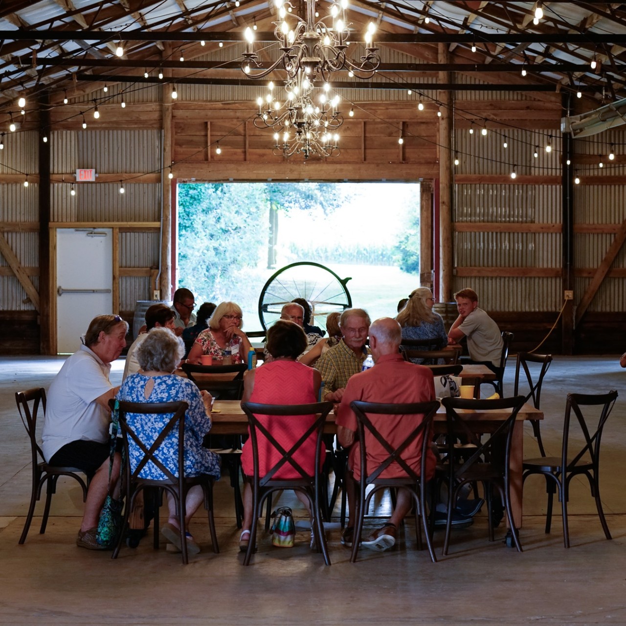 A group of people eating at a table in a beautful decorated barn.