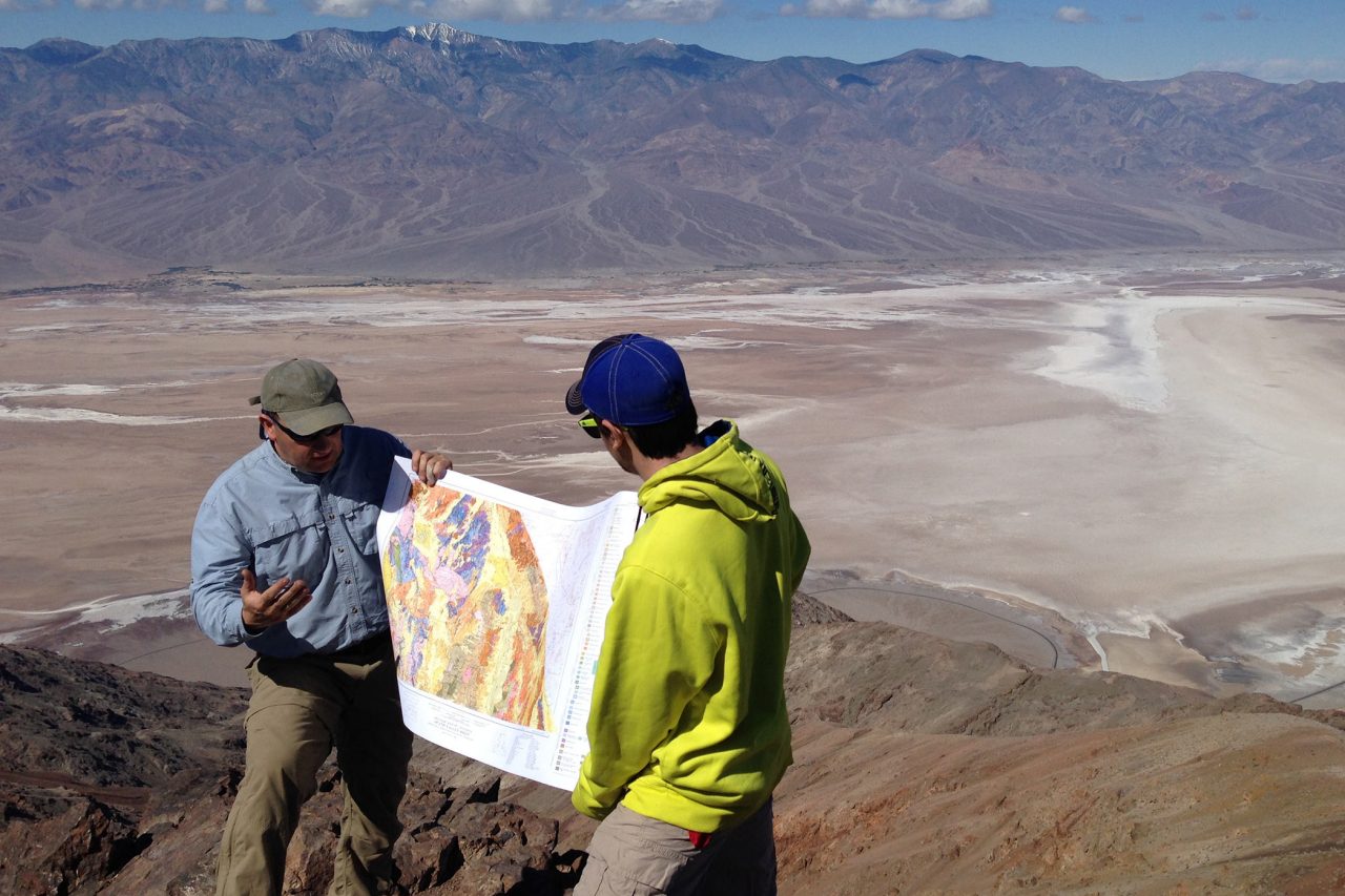 Faculty and student hold open map in front of open landscape