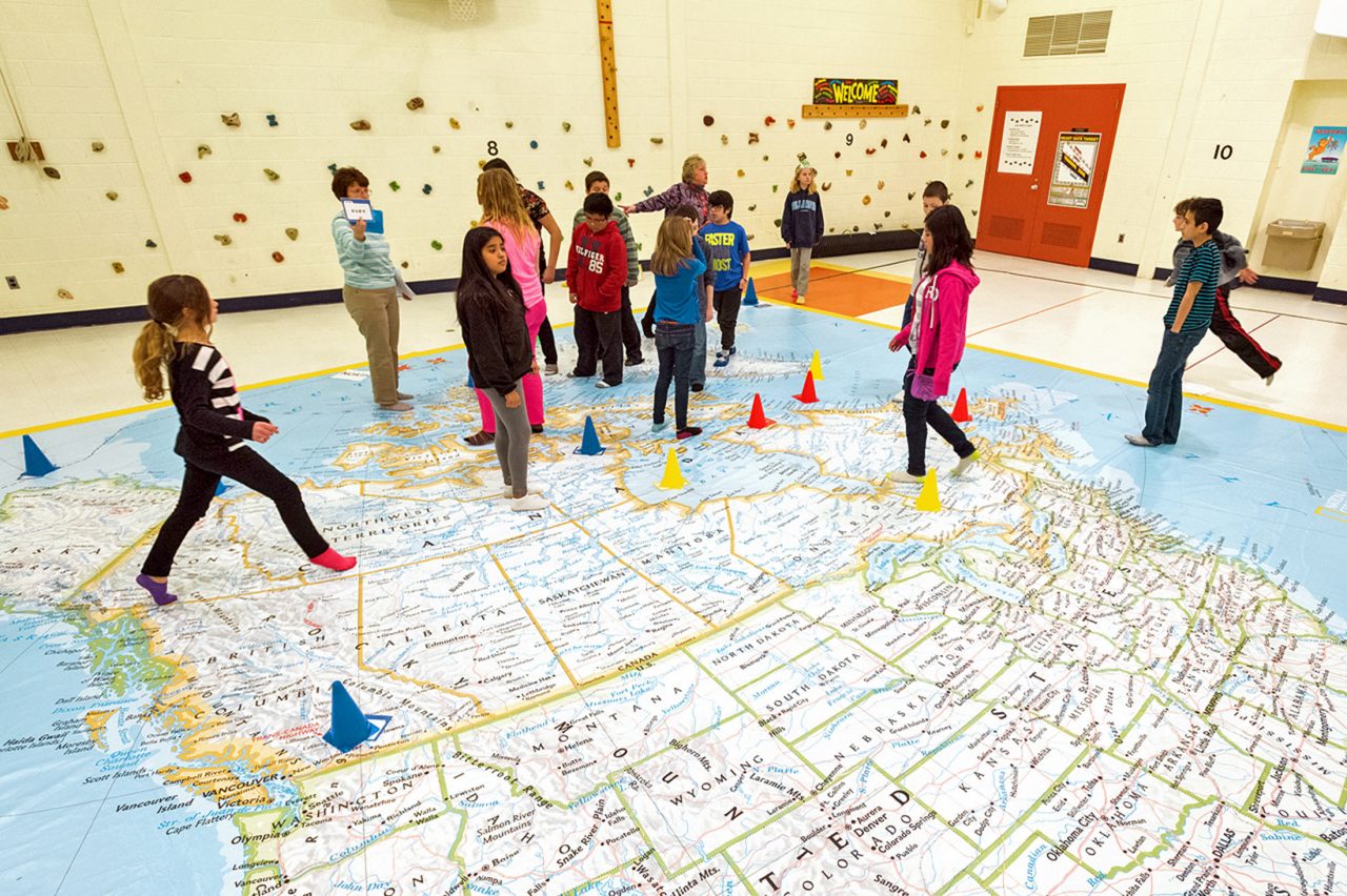 Elementary school students explore a giant map of the US and Canada.