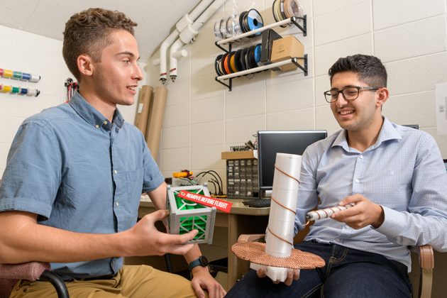 Ahmad Jalal Al Tamini (long sleeve shirt) and Jeffrey Neumann (short sleeve shirt) are undergraduate students working on a Summer Research project to help implement an interface to receive data from the “Cubesat Radio Interferometry Experiment (CURIE).” Lead by researcher Edward Graff (Physics) with Faculty Mentor Bennett Maruca, (Physics and Astronomy) the project aims to develop and deploy a ground station to up- and downlink data with the two CURIE CubeSats which will be making interferometric observations of the Sun. The ground station will be installed at the Mount Cuba Observatory in Wilmington, DE.  Pictured: Jeffrey holds a 3D printed model of a 1:1 scale CubeSat module. The CURIE mission satellies are the same width and length and only 3 times as high.