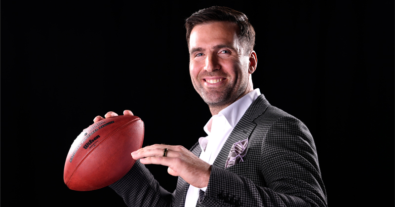 NFL Quarterback, Joe Flacco, poses with a football like he's about to throw it, and smiles for the camera.
