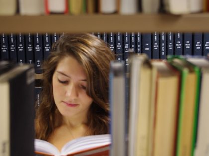 Student reads a book amid the library stacks