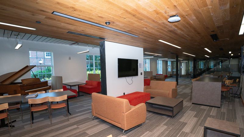 Lounge space with various different tables and chairs around the room. There is a paino in the left side of the picutre and a TV mounted on a wall in the middle of the space.