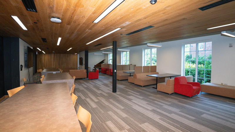 Lounge space with various different tables and chairs around the outside of the room. There is a piano in the back corner.