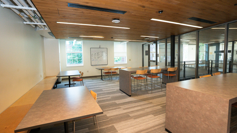 Lounge space with various different tables and seating options, including chairs and benches, around the room. The entire right wall is see-through.