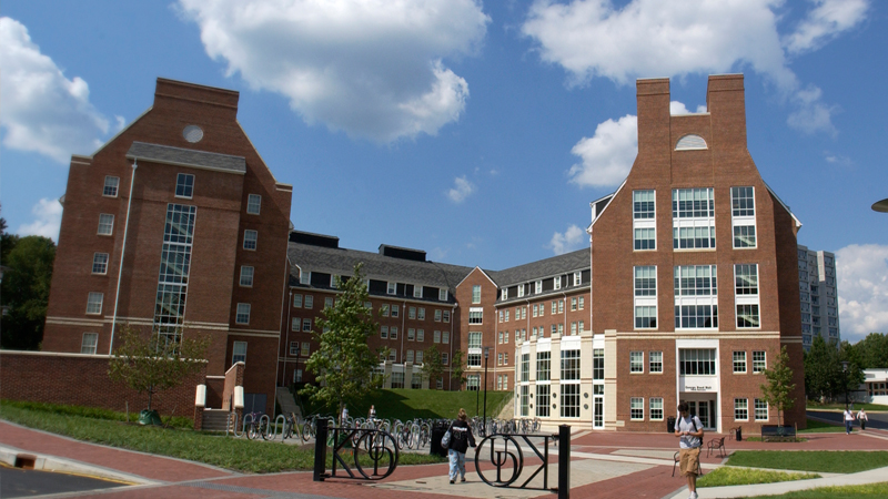 Exterior view of George Read hall, with students walking to and from the building, black gates in front of the building and bike racks to the left.