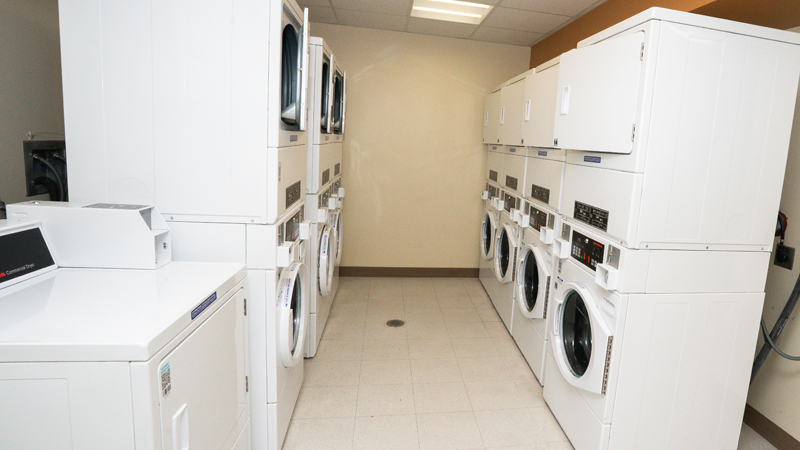 Eight units of stacked washer/dryer units with the washing machines on the bottom and dryers on the top along either side of the picture. There is an additional single dryer unit in front of the stacked units on the left side of the picture.