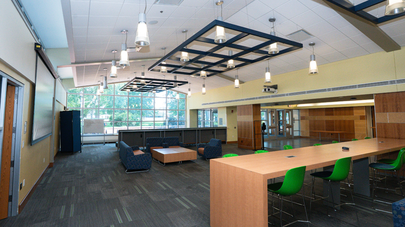 Large, open lounge space with various different tables and seating options around the room. There is a mobile dry erase board in the back of the room and the entire back wall is floor to ceiling windows.