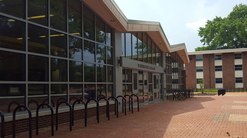 Brick walkway leads up to the entrance of the Harrington Commons with various sets of bike racks in front of the building.