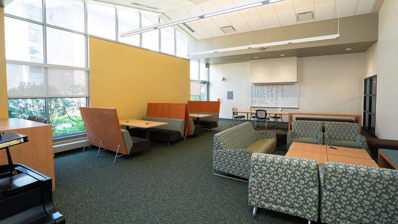 Lounge space with various different tables and chairs around the room. There is a dry erase board mounted on the back wall.