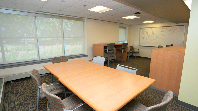 Lounge space with various tables and chairs around the room. There is a dry erase board mounted on the back wall.