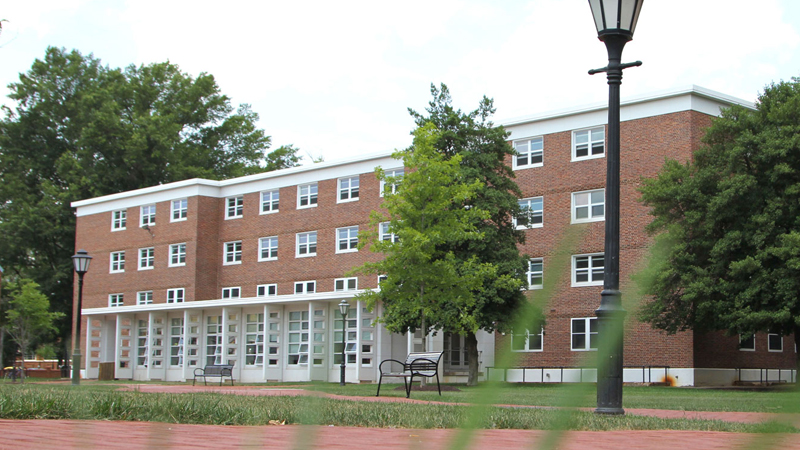 View of front of Thompson hall with a couple picnic benches out front and bike racks to the right of the building. There are a couple trees in front of and to the side of the building as well.