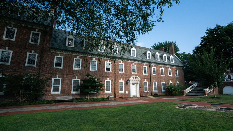 View of the front of Brown Residence Hall from the left, showing the main entrance to the bulding and then a set of stairs to the right that leads to Main Street. There is a brick walkway in front of the building main entrance.