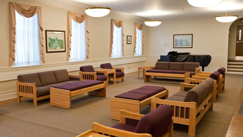 Various lounge chairs and couces around the outside of the room with various side tables and benches, with a piano in the back of the room.