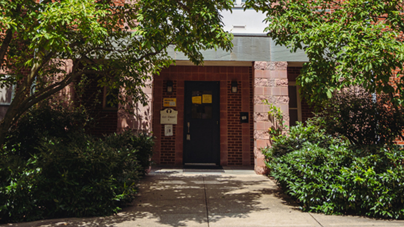 Concrete walkway up to entrance door to Ray C. Greenery and trees surround the walkway and front of the building.