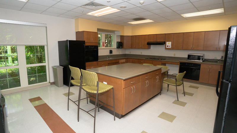 An island sits in the middle of the room with additional cabinet space underneath and chairs around it. There is counter space with cabinets above and below in the back part of the space with a two ovens, a stove and a microwave. There are two refrigerators on either end of the cabinet and counter space.