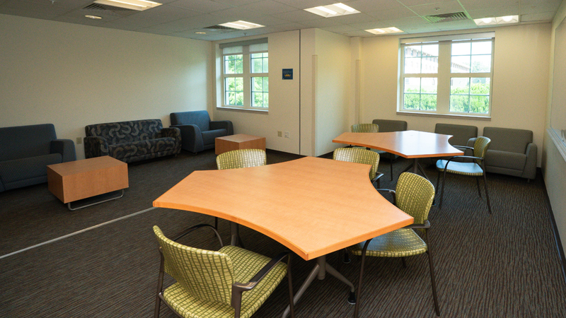 Lounge space with different chairs and tables around the room. There is a dry erase board mounted on the right wall.
