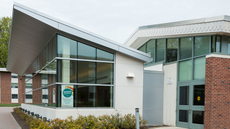 Side view of Russell Dining Hall and Russell Hall E. A brick walkway goes along the front of the dining hall.
