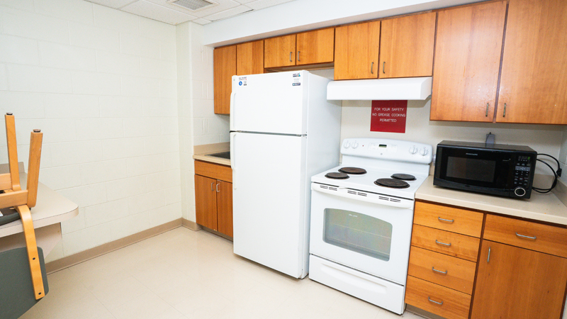 Cabinets with sink, refrigerator, oven and stove, and microwave. Part of a counter space with chairs visible on the left side of the picture.
