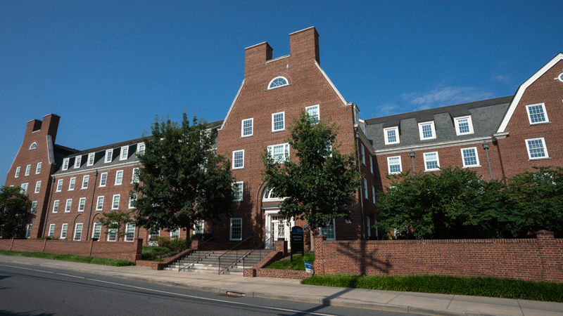 View of the front of the building of South Academy Residence Hall with stairs leading up to the main entrance. There is sidewalk in front of the building, along with multiple trees.