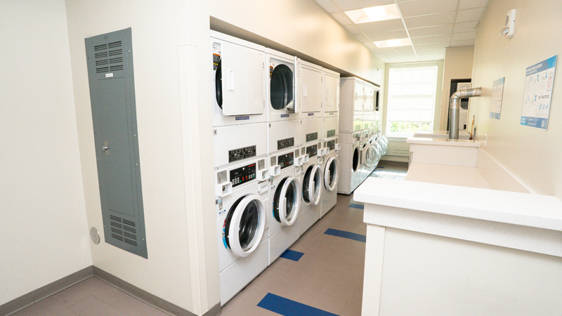 Eight units of stacked washer/dryer units with the washing machines on the bottom and dryers on the top along the left side of the picture. There is a folding shelf on the right side.