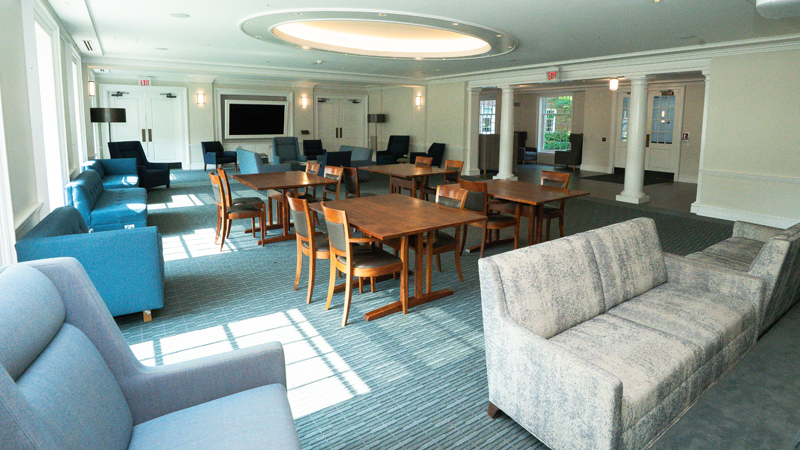 Lounge space with various tables and chairs around the room. There is a projector screen towards the back of the room.