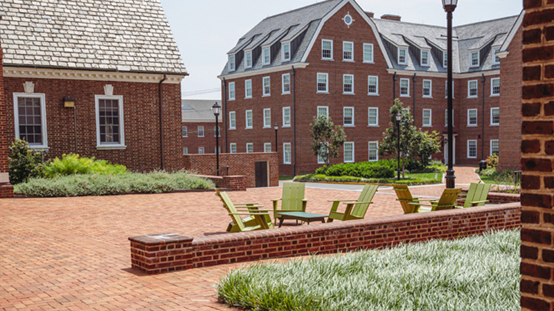 Multiple adirondak chairs and tables sit on the brick patio behind Kent Residence Hall, with a view of South Academy Hall in the back right of the picture.