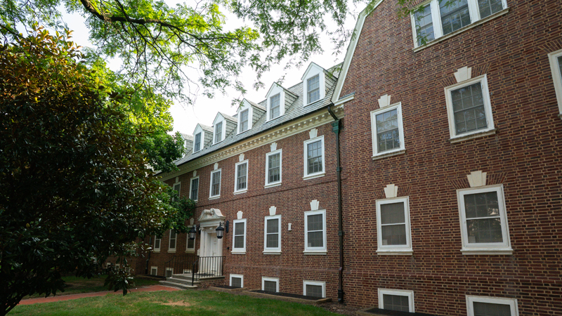 Brick walkway leads up to the main entrance of Squire Residence Hall with various trees in front of the building.