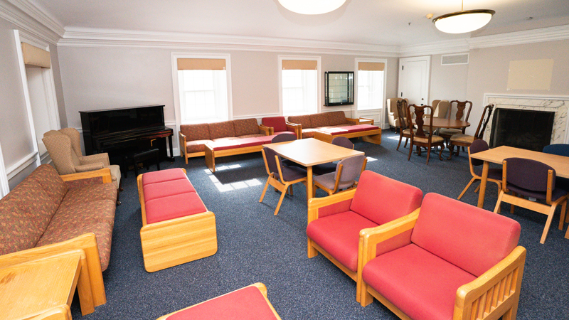 Lounge space with various different tables and chairs around the room. There is a piano in the back corner.