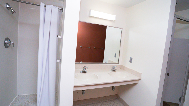 Shower stall with shower curtain on left side of the picture, then two sinks and door to toilet stall on right side.