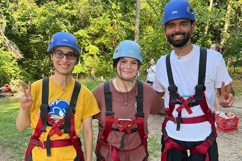 three students in climbing gear pose for a picture