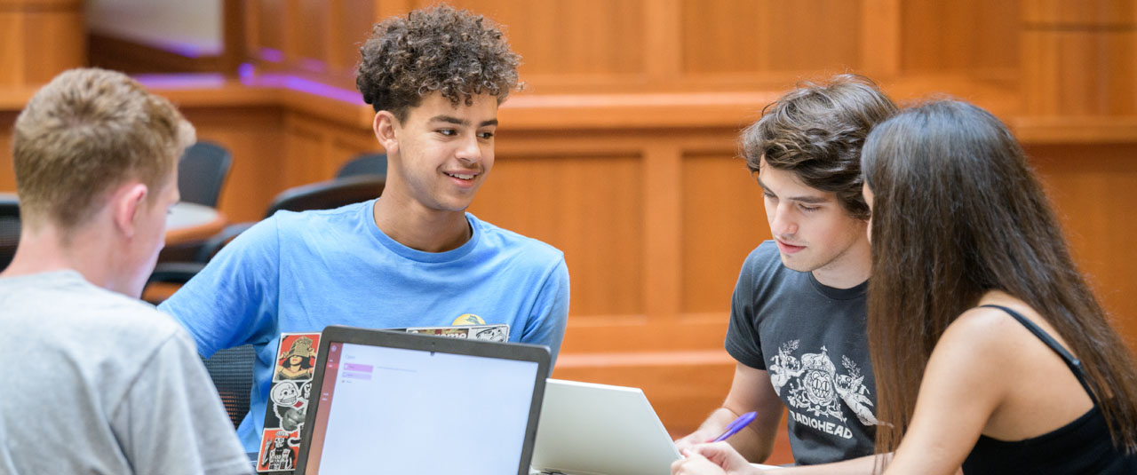 A group of students discussing something over a computer. 