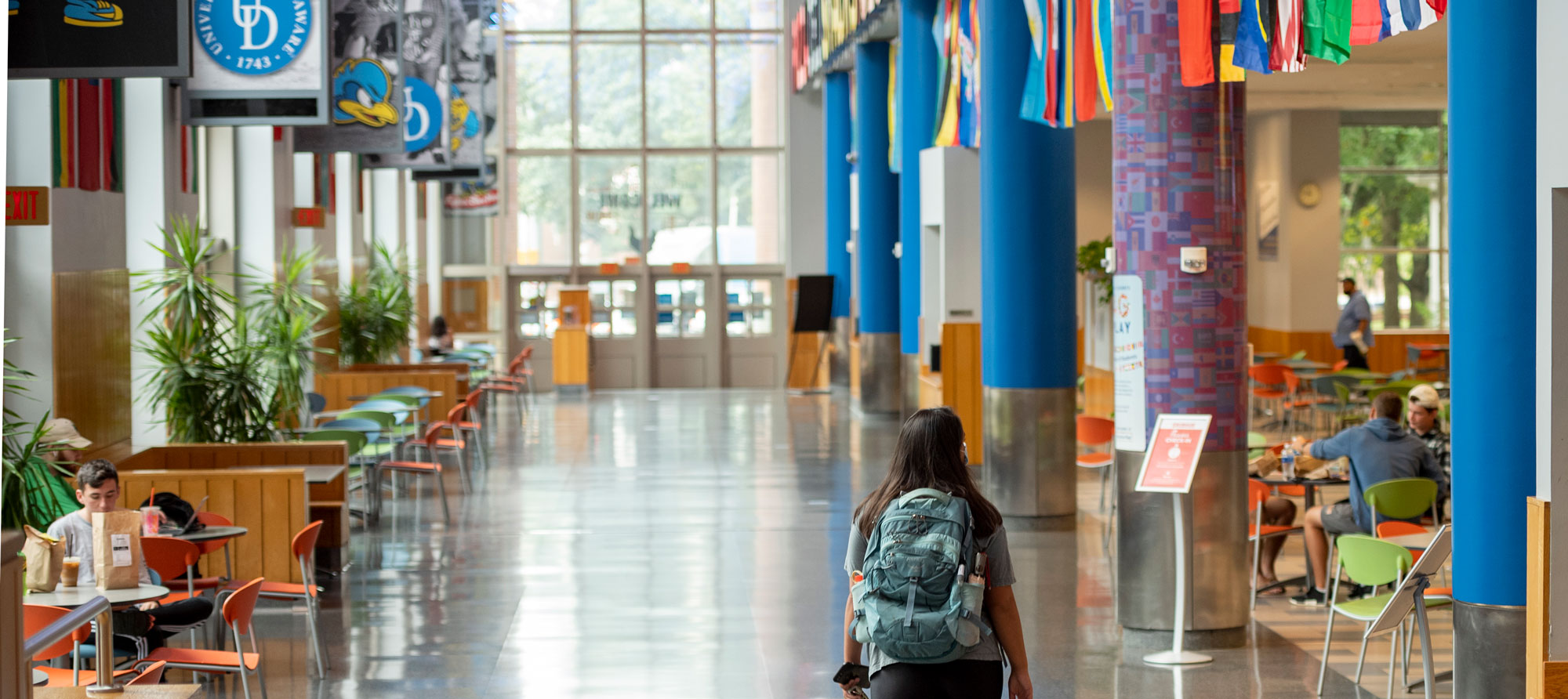 UD student walking through trabant student center with other UD students sitting in the trabant food court