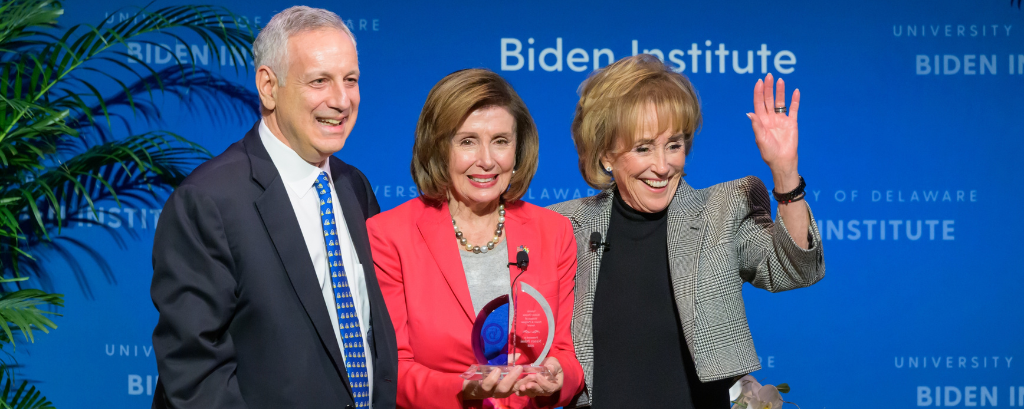 Photo of UD President Dennis Assanis, Speaker Emerita Nancy Pelosi and Biden Institute Chair Valerie Biden Owens stand side-by-side smiling and waving