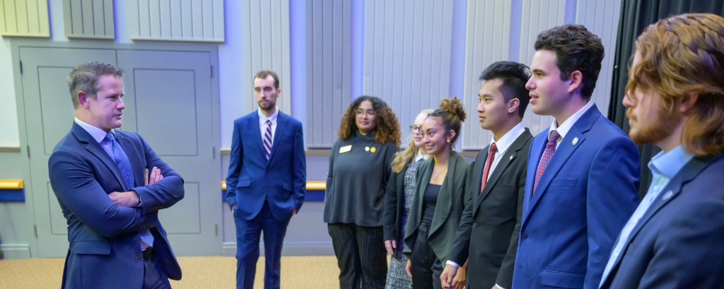 Photo of Adam Kinzinger standing and smiling with crossed arms during a meet-and-greet with Biden Institute student interns