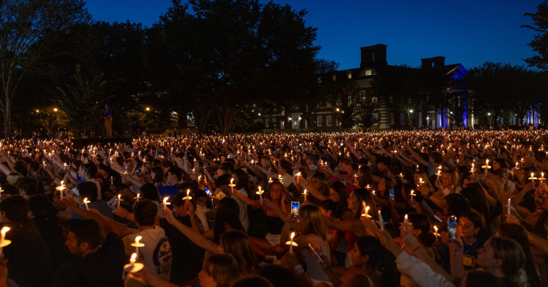 A large group of adults holding candles in the evening light