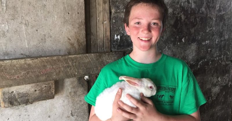 A 4-H member holding a white bunny poses for a photo.
